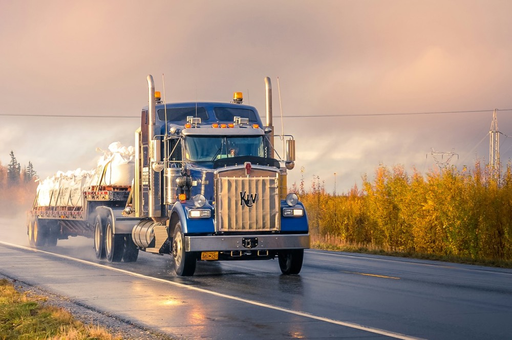 A tractor-trailer running a wet highway at dusk.